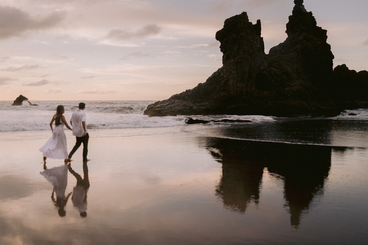 couple running hand in hand on benijo beach at sunset with their reflections in the water